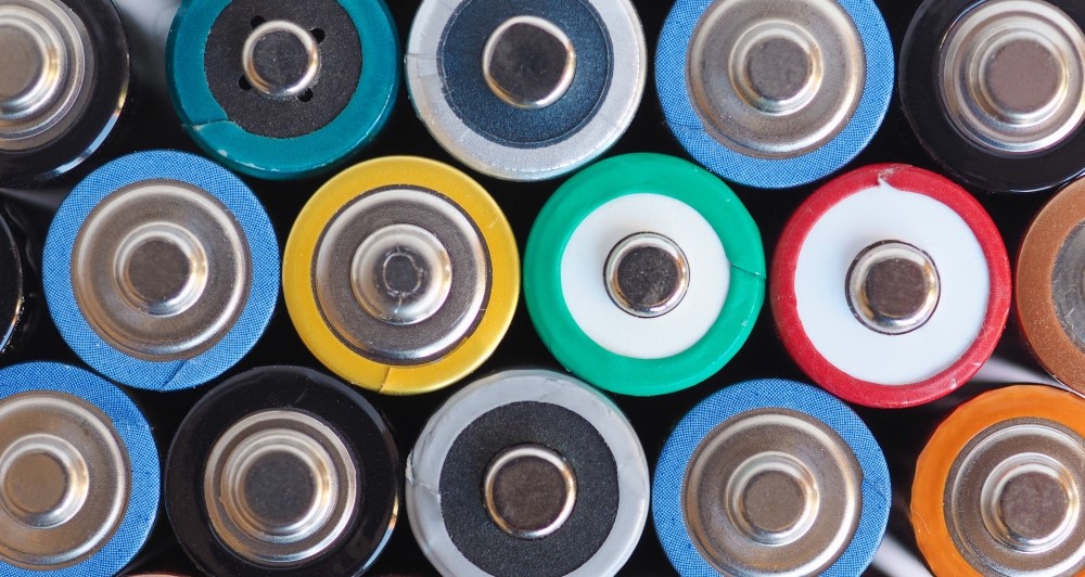 Overhead photo of colorful batteries lined up in three rows showing their positive ends.